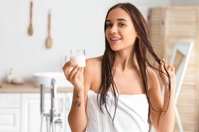 Beautiful young woman with coconut and oil in bathroom