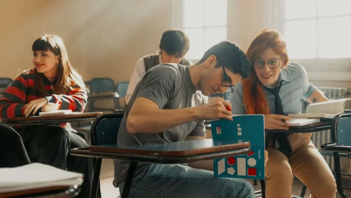 student-rownowaga-nauka-odpoczynek-1 Studenci siedzą w szkolnych ławkach, uczą się i rozmawiają razem.